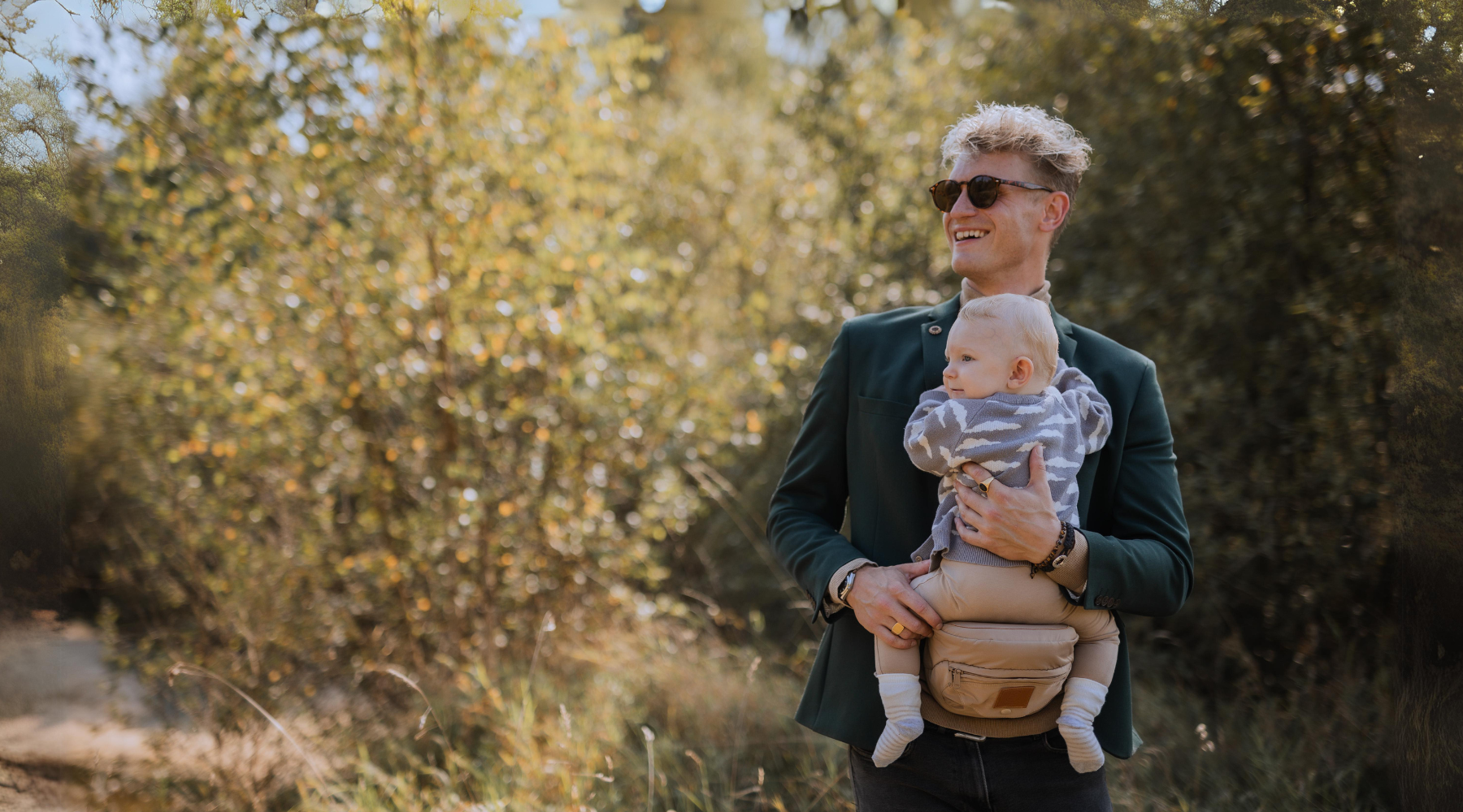 Hoftesæde fra By Minella i neutral farve – praktisk bære-løsning til små børn - Baby sidder trygt og smilende på hoftesæde fra By Minella - Elegant og ergonomisk hoftesæde – must-have baby hack til hverdagen